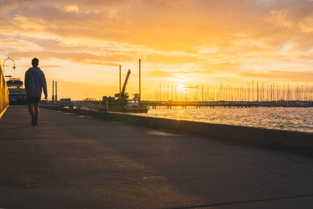 Man walking along the promenade in the port at sunset.の写真素材