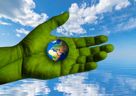 Environment Earth Day. The world turns to climate action. A hand with the texture of a green leaf supports the worldの写真素材