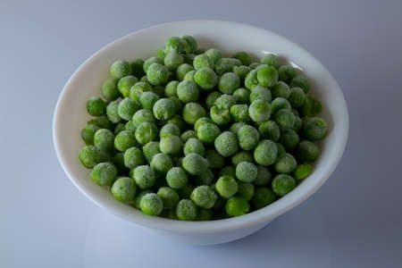 Bowl full of frozen green peas, light background