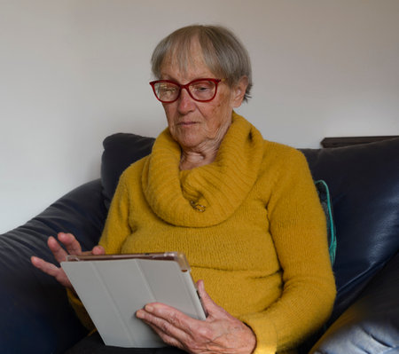 Old mature senior woman using digital tablet looking at computer. Virtual calls, online meetings, watching TV, reading e-books, spending time with technological devicesの写真素材