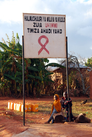 August 2014 - Village of Pomerini - Tanzania - Africa - Some children playing under the sign warning of "country affected by AIDS" at the entrance of the Village of Pomerini.のeditorial素材