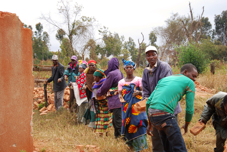 August 18, 2014, Village of Pomerini, Tanzania, Africa - An unidentified group family recovers red clay bricks still usable from a collapsed house in the village Pomerini, using the system of the human chain and pass from hand to handのeditorial素材