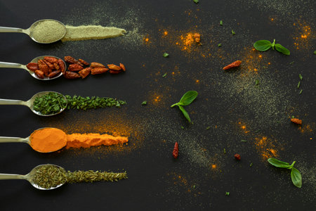 Spoons with spices, pepper, chilli, oregano for dark table