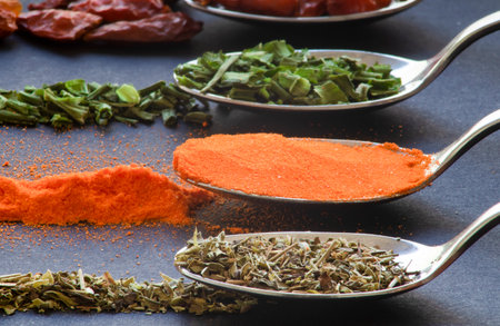 Spoons with spices, pepper, chilli, oregano for dark table