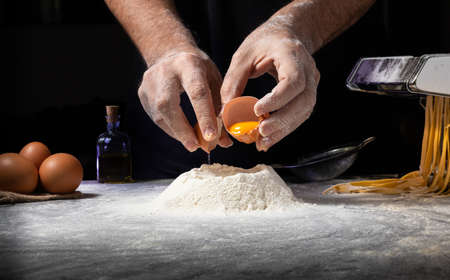 Man making pasta by pouring egg into flour volcano and background with pasta maker and others.