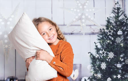 Little girl in red dress at home holding pillow on Christmas datesの写真素材