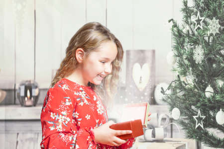 Little girl at home in red dress opening gift box at christmasの写真素材