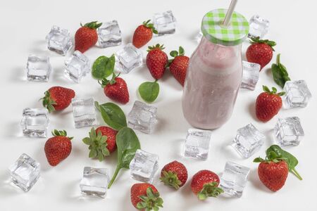 Strawberry smoothie very refreshing for the heat and summer on a white background with ice, fresh strawberries and baby spinach leaves.の写真素材