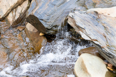 A tranquil stream flowing over smooth rocks, creating small splashes as the water moves around the...