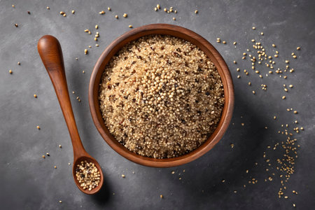 Healthy cooked quinoa grains in a rustic wooden bowl with a matching spoon, set on a textured dark gray surface, highlighting natural color and textureの素材