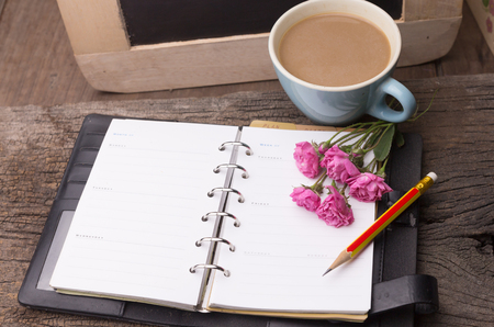 Weekend concept. Pink rose, mug with coffee, diary and pencil on a wooden table. Selective focus, copy space backgroundの写真素材