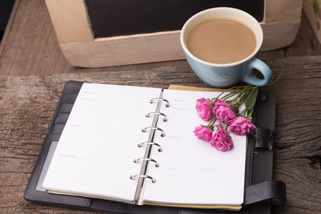 Weekend concept. Pink rose, mug with coffee, diary for note on a wooden table. Selective focus, copy space backgroundの写真素材