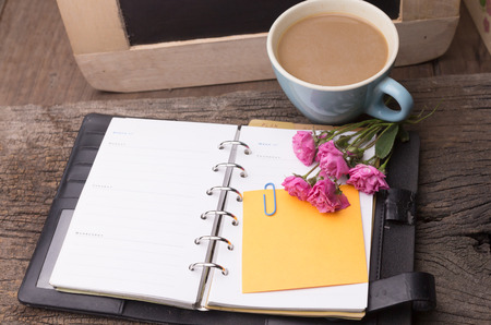 Weekend concept. Pink rose, mug with coffee, diary and stcky notel on a wooden table. Selective focus, copy space backgroundの写真素材
