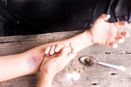 Hand injection drug  with old glass syringe blood, amphetamine tablets and cooked heroin in spoon. on old wood backgroundの写真素材