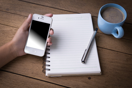 Hand using smartphone,cellphone,tablet over wooden table with notebook and coffee cupの写真素材