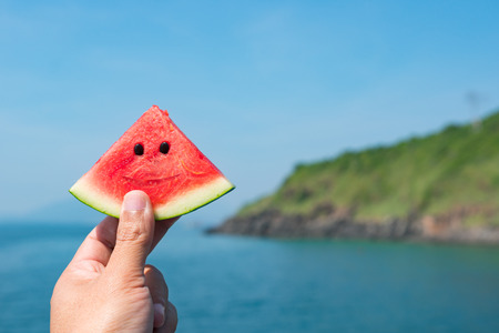 Hand holding a slice of watermelon over an ocean horizonの写真素材