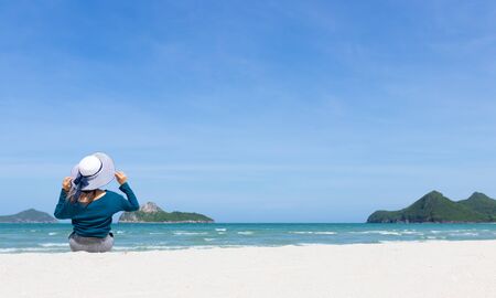 Woman wear summer dress and straw hats sitting on the beach look at sea sky mountain .Time to relax in summer lifestyle outdoor on tropical island beach.concept for Summer time  vacation on the beach.の写真素材