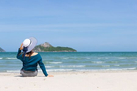 Woman wear summer dress and straw hats sitting on the beach look at sea sky mountain .Time to relax in summer lifestyle outdoor on tropical island beach.concept for Summer time  vacation on the beach.の写真素材