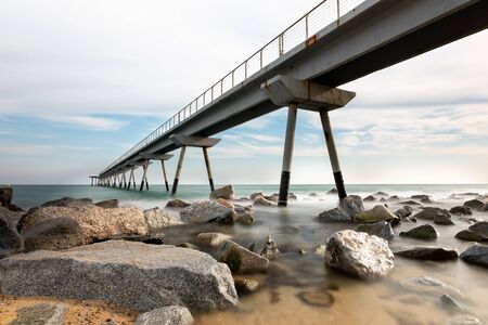 Badalona Oil Bridge, Spain. Panoramic view of the bridge resting on the rocks with water out of focus on them.の写真素材