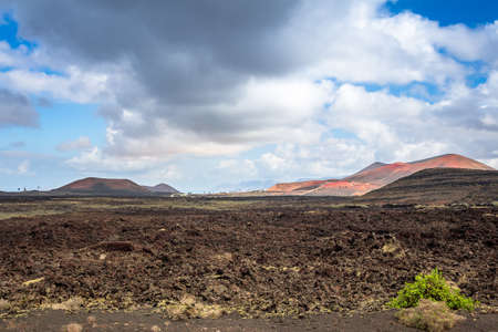 View over a lava field on Lanzarote with red volcanoes in the background, Canary Islands, Spainの写真素材