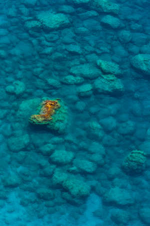 A view of the crystal-clear sea, many rocks under water and a rock jutting out of the waterの写真素材