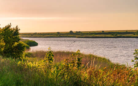 Look across meadows and a sewer in orange glowing dusk, Greetsiel, Germany