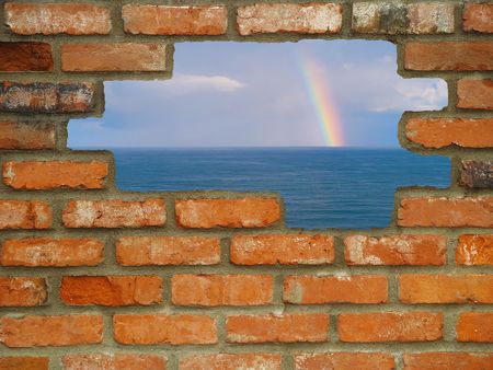 Brick wall background in various shades of red, orange, brown, tan, and white with holes leading from urban to a rainbow on the ocean.の写真素材
