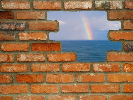 Brick wall background in various shades of red, orange, brown, tan, and white with holes leading from urban to a rainbow on the ocean.の写真素材