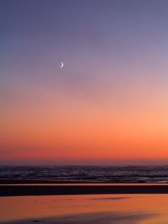 Moonrise over the ocean with a beach foreground        の写真素材