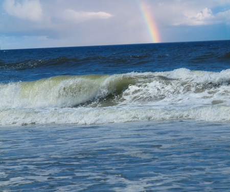 Ocean Waves Breaking on Shore with a Partial Rainbow in the Background  の写真素材