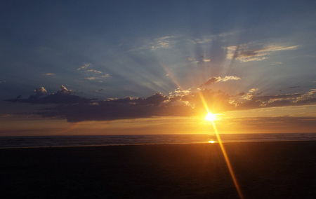 Cloudy Sunset Over the Ocean with Sunbeams in the Skyの写真素材