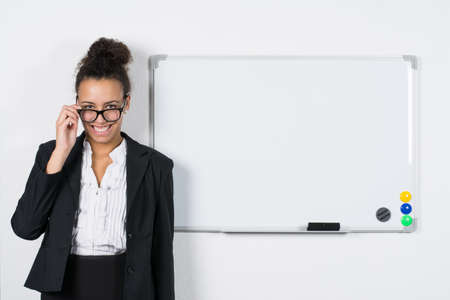 Young office worker stands besides a white magnetic board while holding her glassesの写真素材
