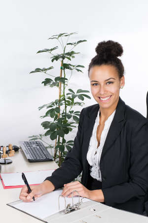 Young office worker writes into a file while sitting at a desk in the officeの写真素材