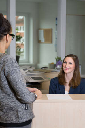 Smiling clerk is sitting behind a counter and is looking to a customer の写真素材