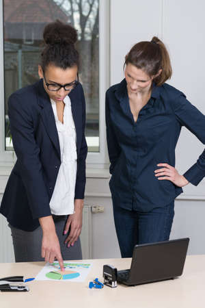 Two young business woman are standing in a meeting. One woman is pointing to a document.の写真素材