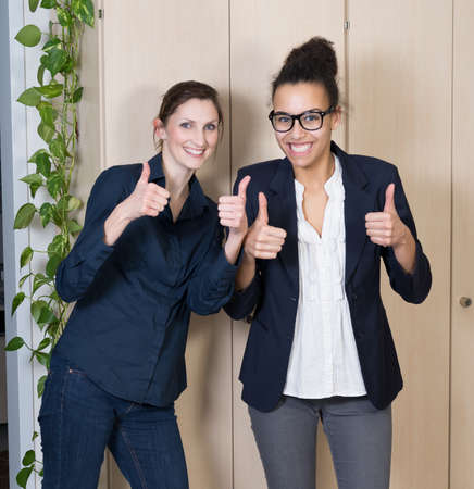 Two businesswomen are standing side by side and are holding her thumbs up.の写真素材