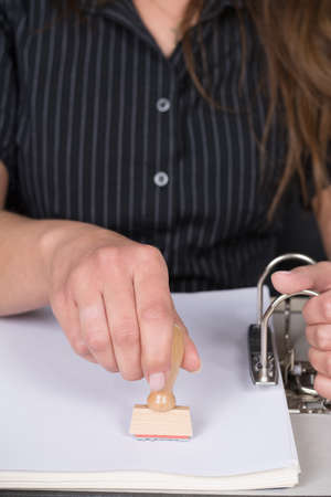 Woman is stamping a document in a file with a stamp at the desk  The stamp is in focus 