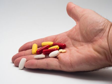 HAND HOLDING A HANDFUL OF COLORED PILLS