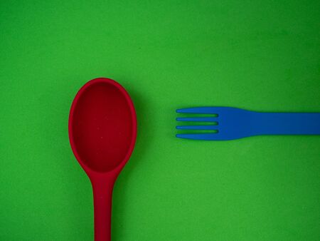 RED SPOON AND BLUE FORK ON GREEN BACKGROUNDの写真素材