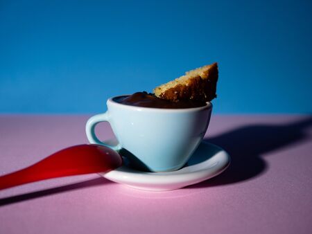 CUP OF CHOCOLATE WITH SPONGE CAKE ON PINK AND BLUE BACKGROUND