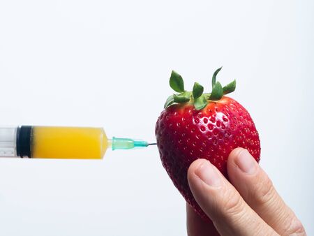 a syringe with orange juice stuck in a strawberry, with white backgroundの写真素材