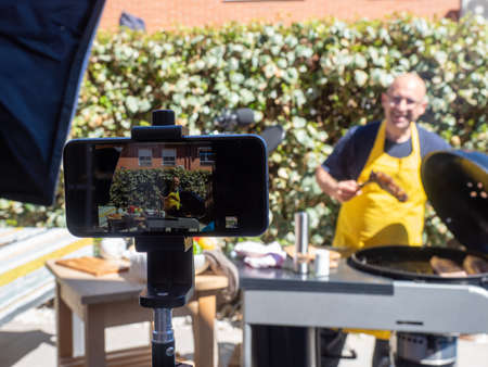 CAUCASIAN MAN IN YELLOW APRON. BARBECUING ON LINE. COOKING COURSE. COOKING IN STREAMINGの写真素材