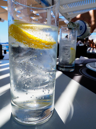 drink and refreshment concept - glass of sparkling water with lemon slices on tableの写真素材
