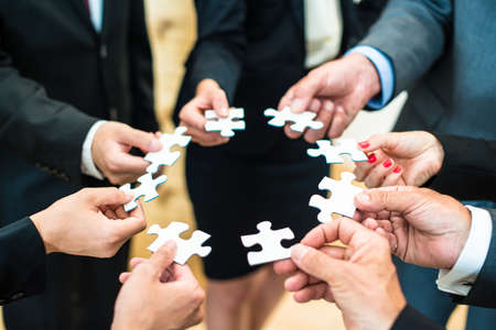 Teamwork - a group of eight business people assembling a jigsaw puzzle - representing team support and help conceptsの写真素材