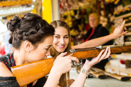 Two attractive girls playing shooting games at German funfairの写真素材