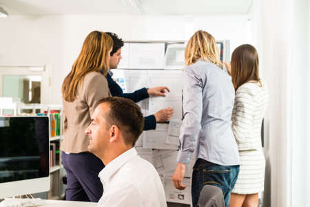 Businesspeople working in the office - some of them looking at bulletin board and discussing designs...
