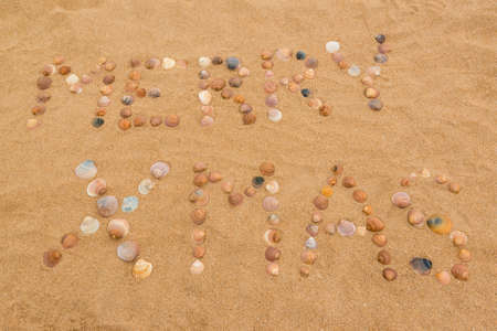 The words Merry Xmas written in the sand on the beach using seashellsの写真素材