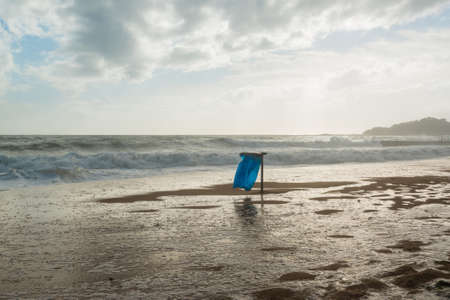 Trash can with blue bag in the waves during high tide on the beachの写真素材