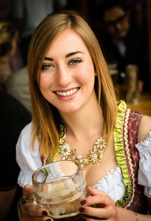 Girl in traditional Dirndl dress is drinking beer while having fun at the Oktoberfestの写真素材