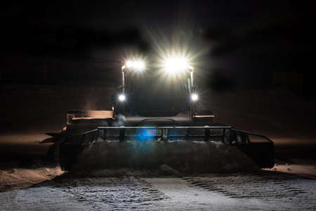 Snowcat preparing a slope at night in high mountains at skiing resortの写真素材